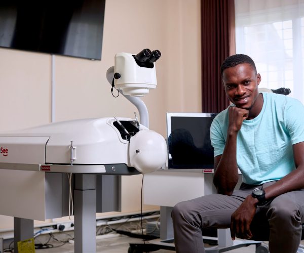 Alagie sits beside a HelpMeSee simulator after completing cataract surgery training.